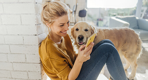 Frau sitzend mit Hund und schaut auf ihr Smartphone